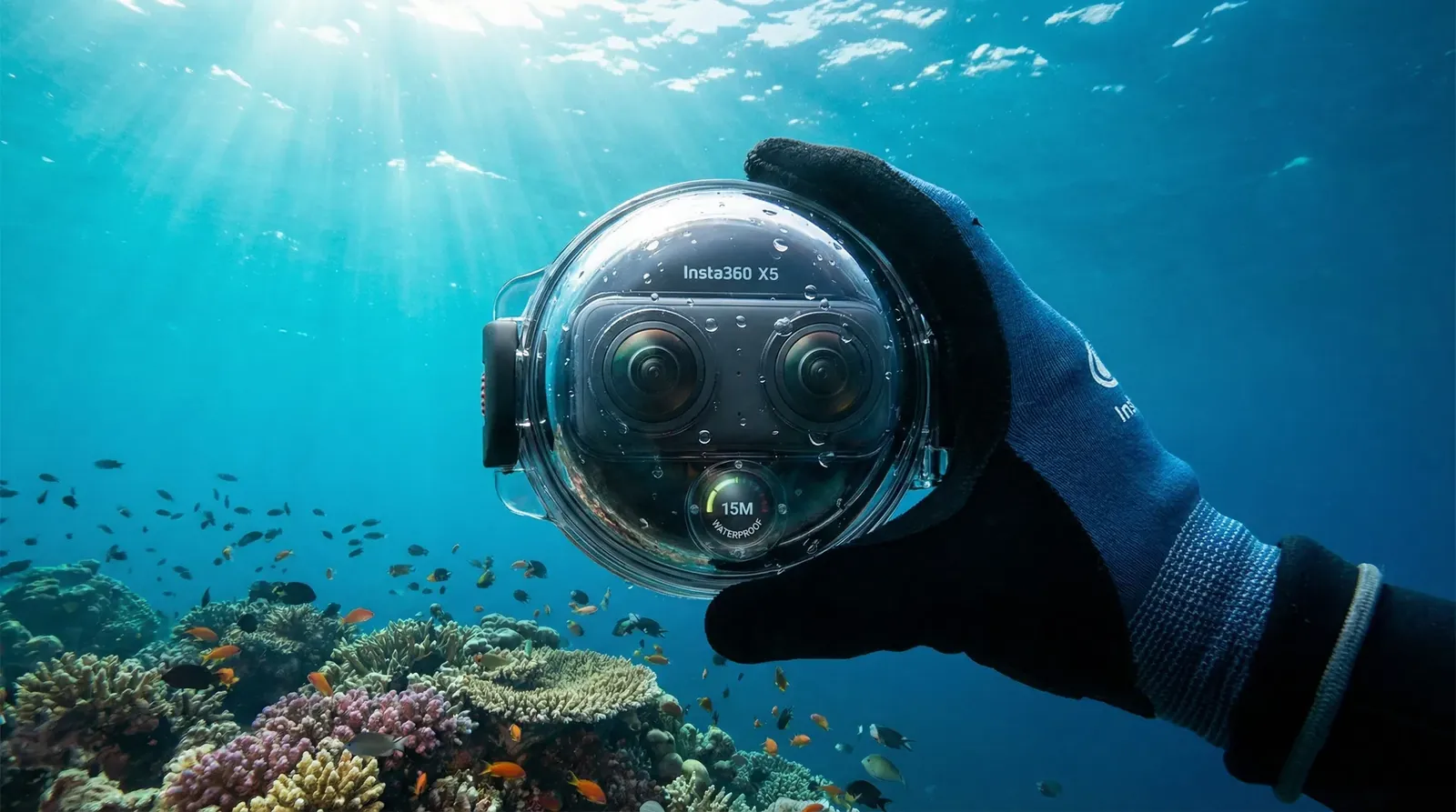 Hand hält eine 360-Grad-Kamera im Tauchgehäuse unter Wasser über einem Riff