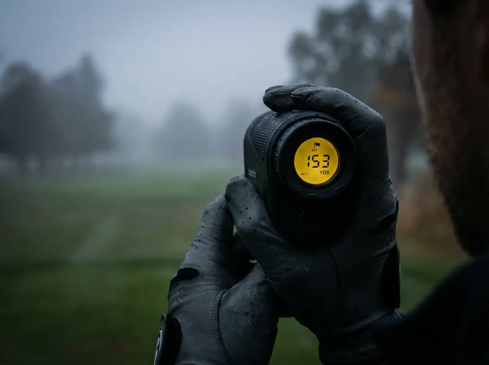 Hand mit Golfhandschuh hält einen Entfernungsmesser im Morgennebel